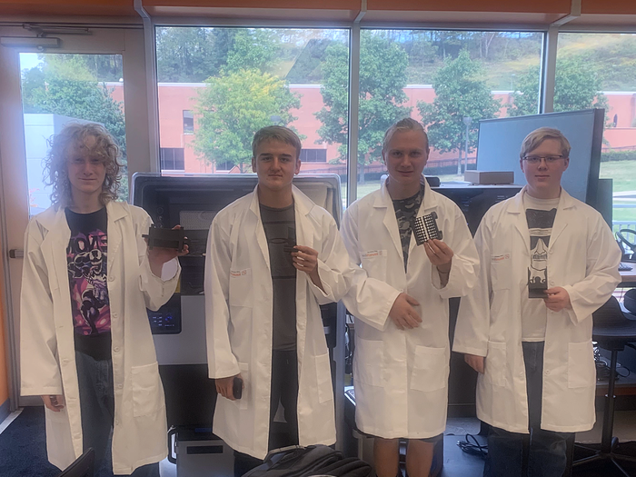 Four students in lab coats holding 3-D printed items