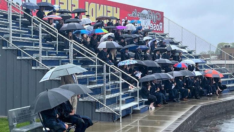 graduating students in bleachers with umbrellas